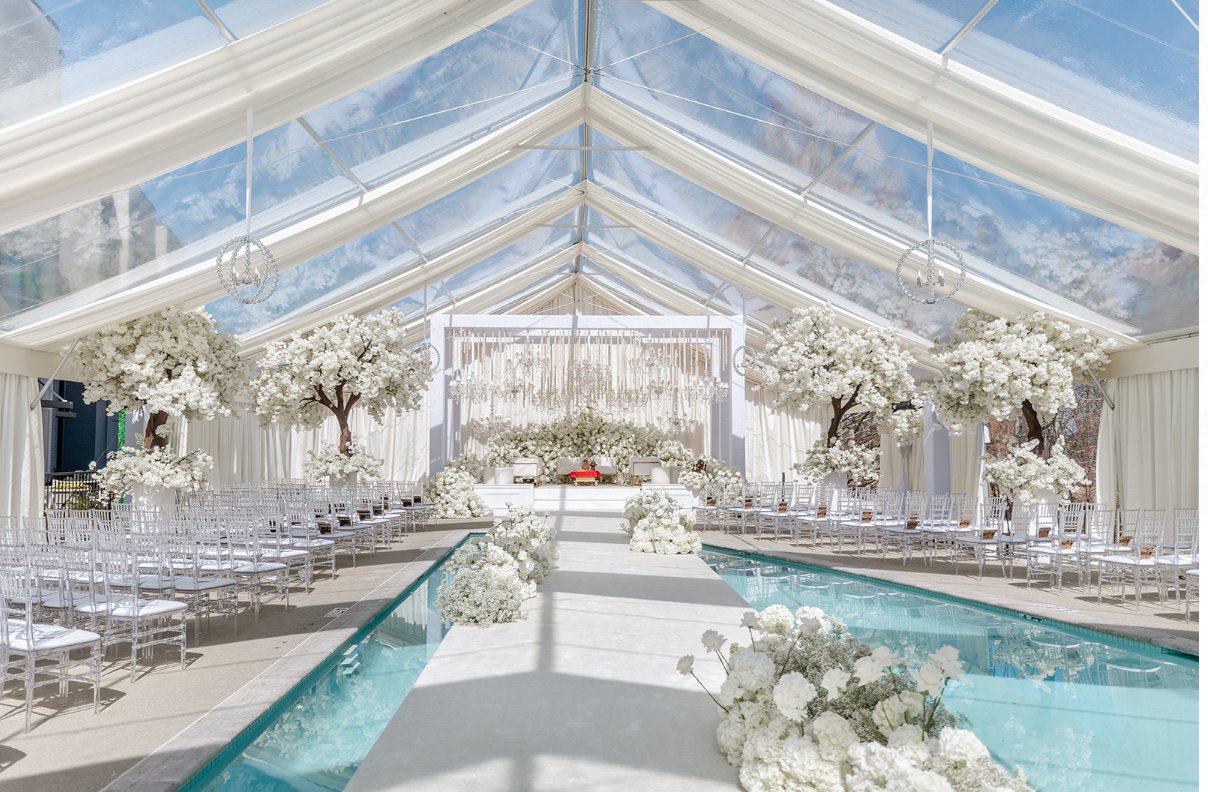 Clear-span tent with white floral trees, crystal chandeliers and pool reflection